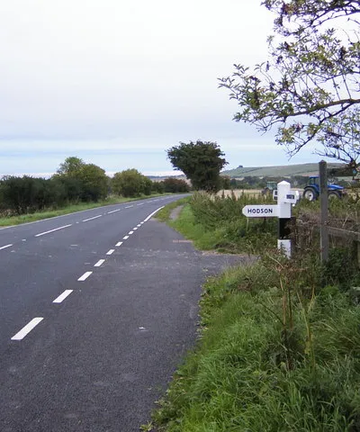Betwix Wroughton and Chiseldon. Standing due south from Hodson, with its turning to our left, and a footpath across the fields to our right. The road ahead goes to Chiseldon, with Liddington Hill and Iron Age Castle in the distance. Tractors are tilling the field just after harvest