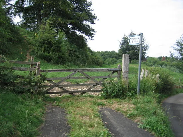 Swerford Motte and Bailey. The sign point directly toward the Motte with the Bailey partially hidden in the bushes and trees.