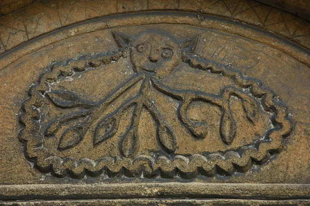 'Cat o' nine tails', Dumbleton Church, near to Dumbleton, Gloucestershire, Great Britain.
This carving is on the tympanum above the north door to Dumbleton church. In the book, 'The Blacksmith's Daughter' by Susan Oldacre, this carving is called the 'Cat o' nine tails'. Pevsner describes it as: 'crudely carved (or recut) with leaves issuing from a grotesque's mouth'.