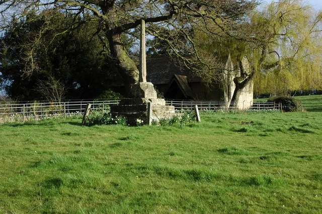 Base and shaft of a Medieval stone cross at Wick, Worcestershire, with St Mary's parish church visible through the trees