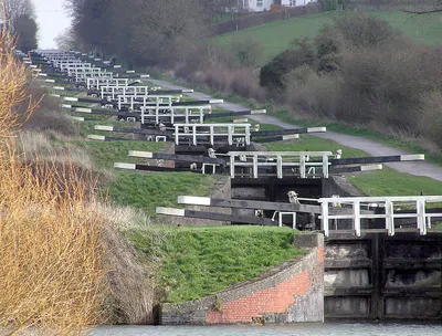 The Caen Hill locks, on the Kennet and Avon Canal, Devizes, Wiltshire, England, in early Spring. The sixteen locks of Caen Hill (seen in this picture), and a further 13 locks, stretch over only 2 miles of the canal. The large side ponds are not seen here. The white "fences" are bridges across each lock.
The building of these locks in 1810 marked completion of the whole 57 mile distance from Newbury to Bath. 
Photographed by Adrian Pingstone in March 2007 and placed in the public domain.
Other versions: