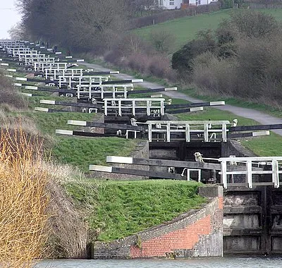 The Caen Hill locks, on the Kennet and Avon Canal, Devizes, Wiltshire, England, in early Spring. The sixteen locks of Caen Hill (seen in this picture), and a further 13 locks, stretch over only 2 miles of the canal. The large side ponds are not seen here. The white "fences" are bridges across each lock.
The building of these locks in 1810 marked completion of the whole 57 mile distance from Newbury to Bath. 
Photographed by Adrian Pingstone in March 2007 and placed in the public domain.
Other versions: