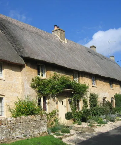 33 and 35 Taynton, Oxfordshire: a pair of thatched 18th-century cottages opposite Manor Farm. 35 in the foreground has a modern extension in a traditional Cotswold style.