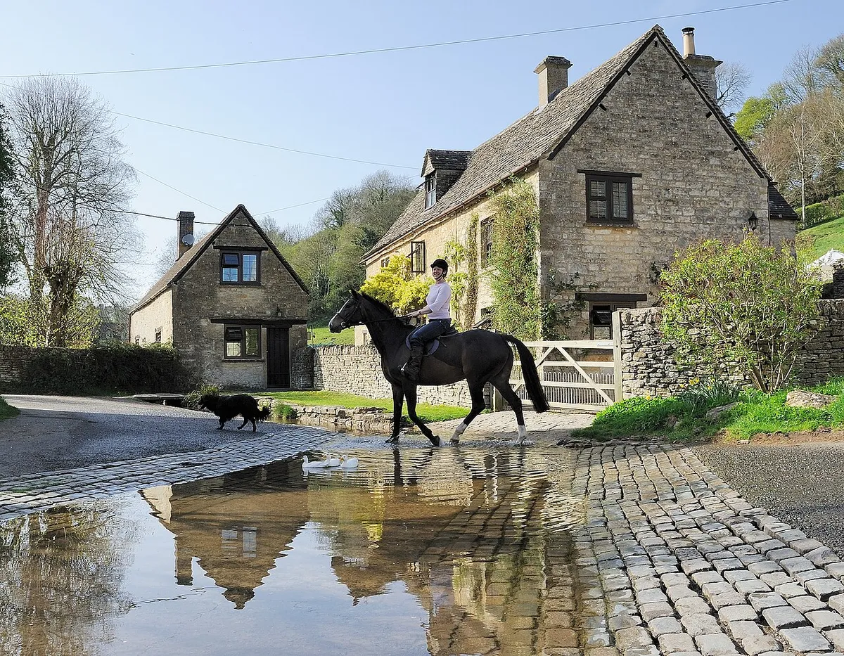 A rider and her dog cross the River Dunt through the ford at Duntisbourne Leer. Duntisbourne Leer is a Cotswolds village located in Gloucestershire approximately 5 miles northwest of Cirencester. .mw-parser-output .messagebox{margin:4px 0;width:auto;border-collapse:collapse;border:2px solid var(--border-color-progressive,#6485d1);background-color:var(--background-color-neutral-subtle,#fbfcff);color:var(--color-base,#202122);box-sizing:border-box;border-inline-start-width:8px}.mw-parser-output .messagebox.mbox-small{font-size:88%;line-height:1.25em}.mw-parser-output .mbox-warning,.mw-parser-output .mbox-speedy{border:2px solid var(--border-color-error,#b22222);background:var(--background-color-error-subtle,#ffdbdb);border-inline-start-width:8px}.mw-parser-output .mbox-serious,.mw-parser-output .mbox-delete,.mw-parser-output .mbox-stop{border:2px solid var(--border-color-error,#b22222);border-inline-start-width:8px}.mw-parser-output .mbox-issue,.mw-parser-output .mbox-content{border:2px solid #f28500;background:var(--background-color-warning-subtle,#ffe);border-inline-start-width:8px}.mw-parser-output .mbox-query,.mw-parser-output .mbox-style{border:2px solid #f4c430;background:var(--background-color-warning-subtle,#ffe);border-inline-start-width:8px}.mw-parser-output .mbox-shit{border:2px solid #960;border-inline-start-width:8px}.mw-parser-output .mbox-license{border:2px solid #88a;border-inline-start-width:initial}.mw-parser-output .mbox-legal{border:2px solid var(--border-color-notice,#666);background:var(--background-color-base,#fff);border-inline-start-width:8px}.mw-parser-output .mbox-honor{border:2px solid #ca3;background:var(--background-color-warning-subtle,#fcf4db);border-inline-start-width:8px}.mw-parser-output .mbox-growth{border:2px solid #8d4;background:var(--background-color-success-subtle,#d5fdf4);border-inline-start-width:8px}.mw-parser-output .mbox-move{border:2px solid #93c;border-inline-start-width:8px}.mw-parser-output .mbox-protection,.mw-parser-output .mbox-message{border:2px solid var(--border-color-base,#aaa);border-inline-start-width:8px}.mw-parser-output .messagebox .mbox-text{border:none;padding:0.25em 0.9em;width:100%}.mw-parser-output .messagebox .mbox-image{border:none;padding:2px 0 2px 0.9em;text-align:center}.mw-parser-output .messagebox .mbox-imageright{border:none;padding:2px 0.9em 2px 0;text-align:center}.mw-parser-output .messagebox .mbox-empty-cell{border:none;padding:0;width:1px}.mw-parser-output .messagebox .mbox-invalid-type{text-align:center}@media(min-width:720px){.mw-parser-output .messagebox{margin:4px 10%}.mw-parser-output .messagebox.mbox-small{clear:right;float:right;margin:4px 0 4px 1em;width:238px}}body.skin--responsive .mw-parser-output table.messagebox img{max-width:none!important}Wikidata has entry Leigh Cottage (Q26380861) with data related to this item.Wikidata has entry Turner's (Q26592314) with data related to this item.