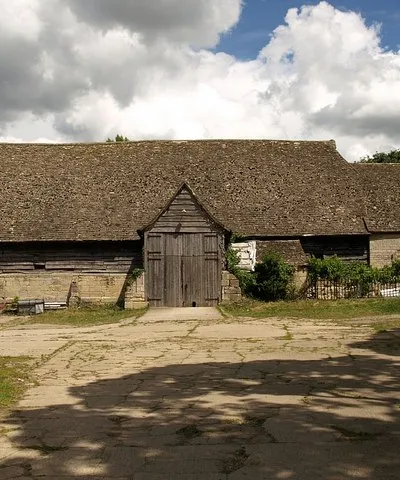 Barn, Upton St. Leonards This magnificent barn is at Manor Farm, on Portway. The following description is taken from the description on http://www.stroud.gov.uk/info/listed_buildings/upton_stleonards.pdf :
"Large barn with attached stable at east end. C15, possibly
earlier; late C17 stable. Very large coursed and squared
limestone; timber framing; coursed rubble to stable; stone slate
roof (clay pantile to north slope). Off-centre south porch to 6-
bay barn; stable with loft. South side: stone base walls with
chamfered plinth and buttresses; gabled porch with plank barn doors
and outshut to right; weatherboarded porch gable and upper part of
barn walls; low opening in wall to left of porch with plank doors;
plain stone side wall to stable. East end: barn end is half-hipped
with small gablet, gabled stable with 2 stable doors having timber
lintels; central loft door over with timber lintels; 3 rows of
a pigeon holes in gable apex. North side: weatherboarded above
buttressed stone base walls as to south; central porch with raised
sprocketted roof; attached shelter sheds are not of special
interest. West end: weatherboarded half-hipped gable end with
I 3 gablet above buttressed stone base wall.
S= Interior has 7 raised cruck trusses with very high cambered collars
and arched bracing; 2 rows of purlins and ogee-curved wind bracing:
close studded end walls; small framing along sides. Internal span Il of approximately 8.2m across feet of crucks. Rafters and framing
are original: C15 work is largely intact with little evidence of
repair or replacement. C19 iron tie-rods sag and appear
unnecessary. A lofty and elegant structure. Important barn and
one of the best in the county. Possibly built as Tithe Barn for Gloucester Abbey. (N.W. Alcock, Cruck Construction: An Introduction and Catalogue, Q 1981).