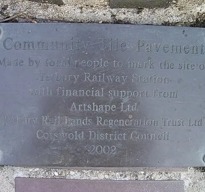 Commemorative plaque marking the site of Tetbury Railway Station Community Tile Pavement.
Made by local people to mark the site of
Tetbury Railway Station
with financial support from
Artshape Ltd
Tetbury Rail Lands Regeneration Trust Ltd
Cotswold District Council
2002.
The plaque is located on the site of the former G.W branch line terminus at Tetbury, the line from Kemble Junction to Tetbury was opened in 1889 it final closed in 1964 after serving Tetbury for 74 years. The red brick station building was demolished during the early 1970s.