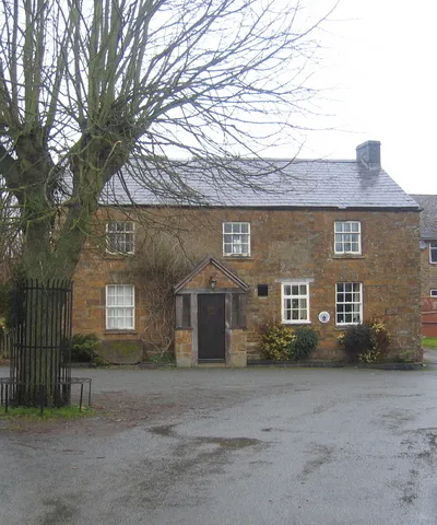 The former Sunrising Inn, Church Lane, Claydon, Oxfordshire, seen from the south. It closed in 1990 and is now a private house. The white and blue circular glazed plaque between the windows on the ground floor shows it was once a tied house of the Hunt Edmunds brewery of Banbury.