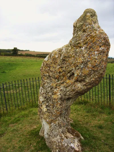 The King Stone at Rollright, a tall twisted standing stone inside iron railings, with fields behind