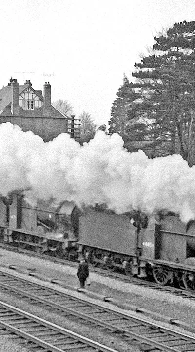 Two light engines coupled heading towards Cheltenham.
View SW, towards Gloucester etc. from a bridge over the railway, Churchdown station being off to the right: ex-GW & Midland Joint Cheltenham - Gloucester main line (see other Churchdown scenes for details of routes along this busy stretch, which was quadrupled 1942 - 1967). Two LMS Fowler 4F 0-6-0s, Nos. 44454 (1928 - 10/63) and 44179( 1925 - 12/64) are passing my Morris Oxford parked in the road above.